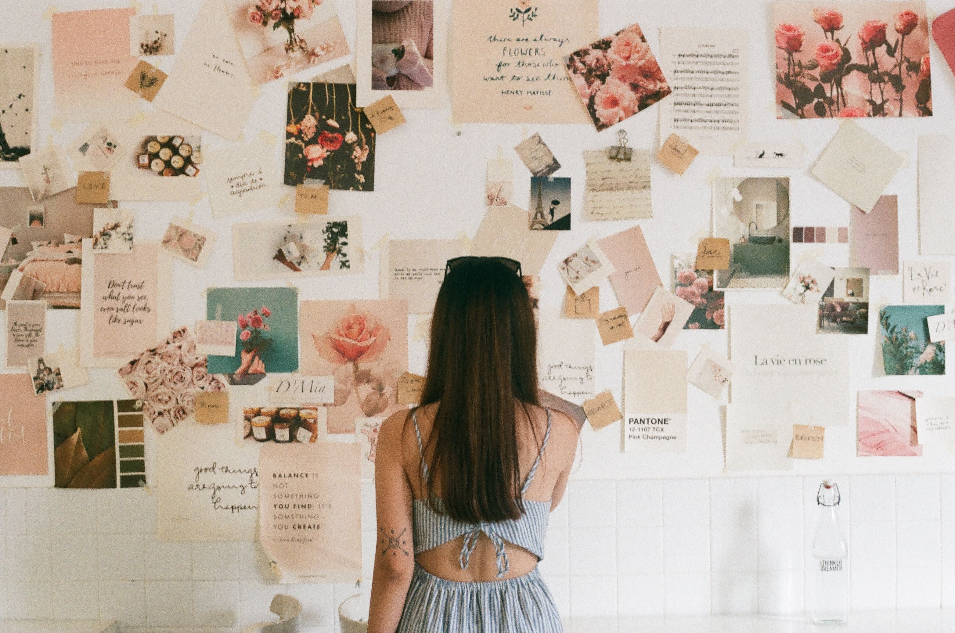 Femme de dos devant un mur couvert d'un vision board rose et floral, avec citations, photos et échantillons de couleurs Pantone.